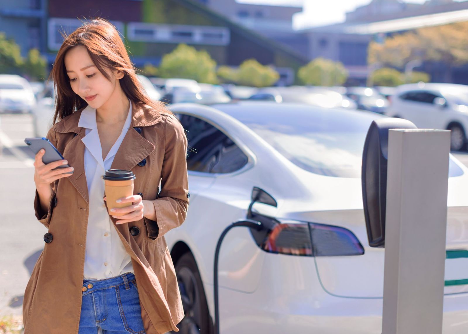 Donna con lo smartphone accanto a un’auto elettrica in ricarica
